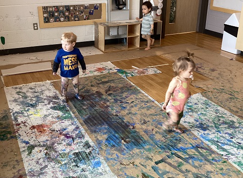 Infants standing in the messy paint covered room