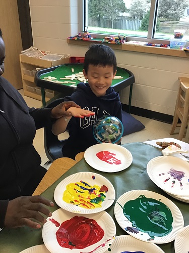 A child and an educator at a table painting handprints