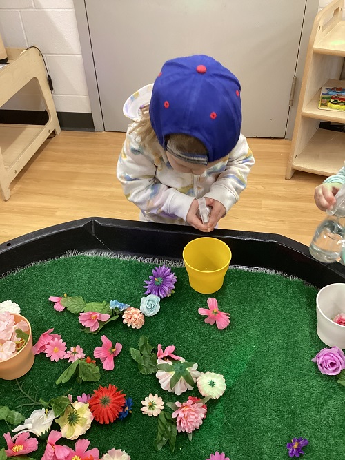 A toddler child using a spray bottle to water artificial flowers