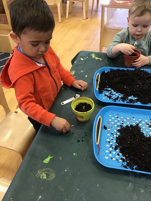 Children putting soil in their flower pot.