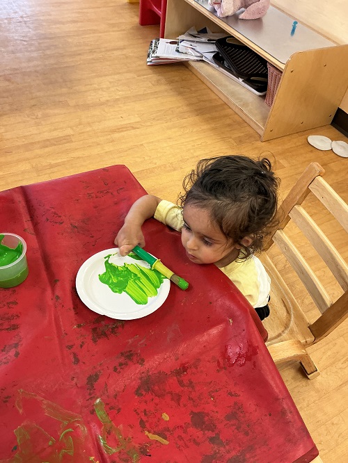 Child painting a paper plate green.