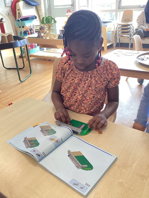 A preschool child following directions in the lego book while building with lego
